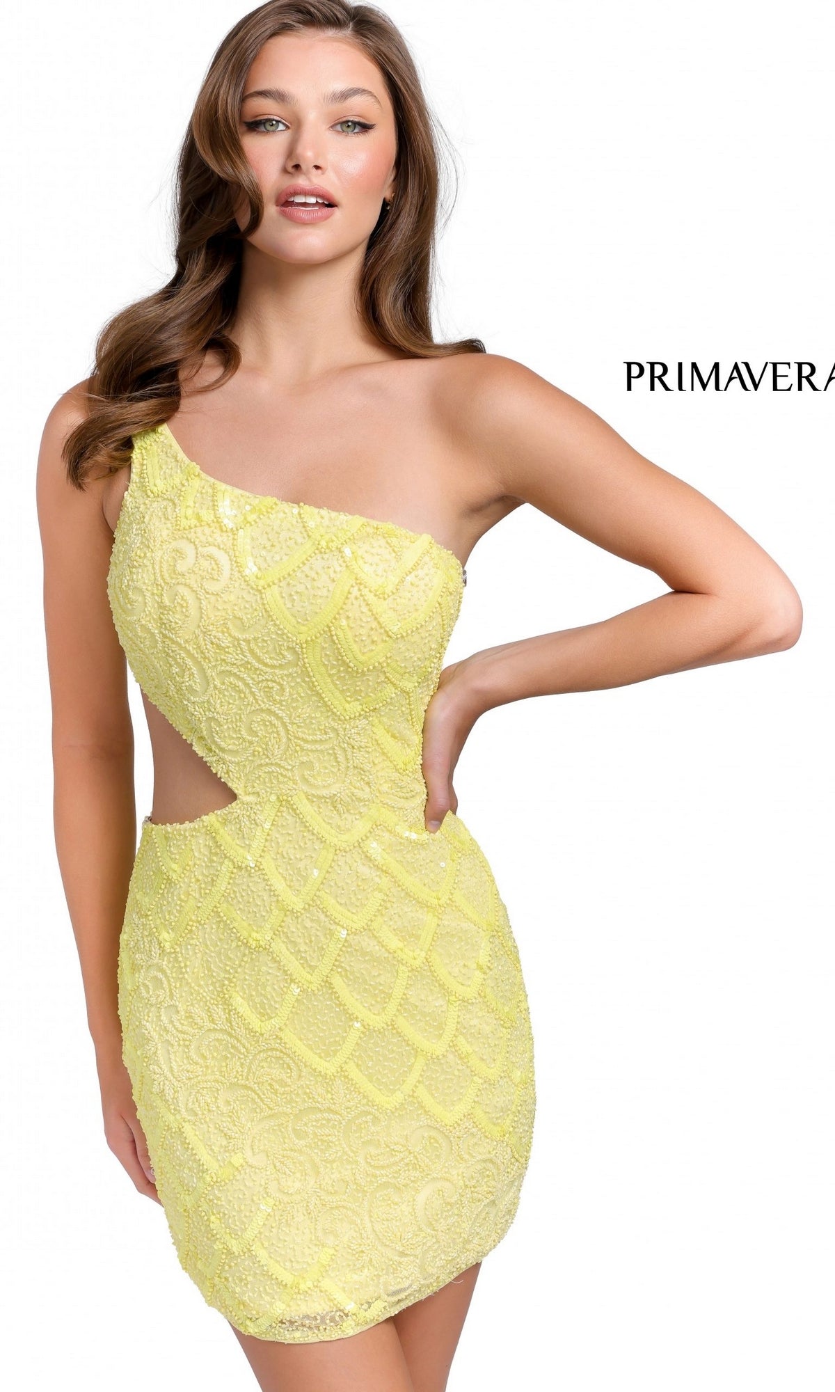 A woman poses with one hand on her hip in the Primavera 3504B—an eye-catching, yellow, one-shoulder short party dress featuring sparkling beads, sequins, and a stylish side cut-out against a plain background.